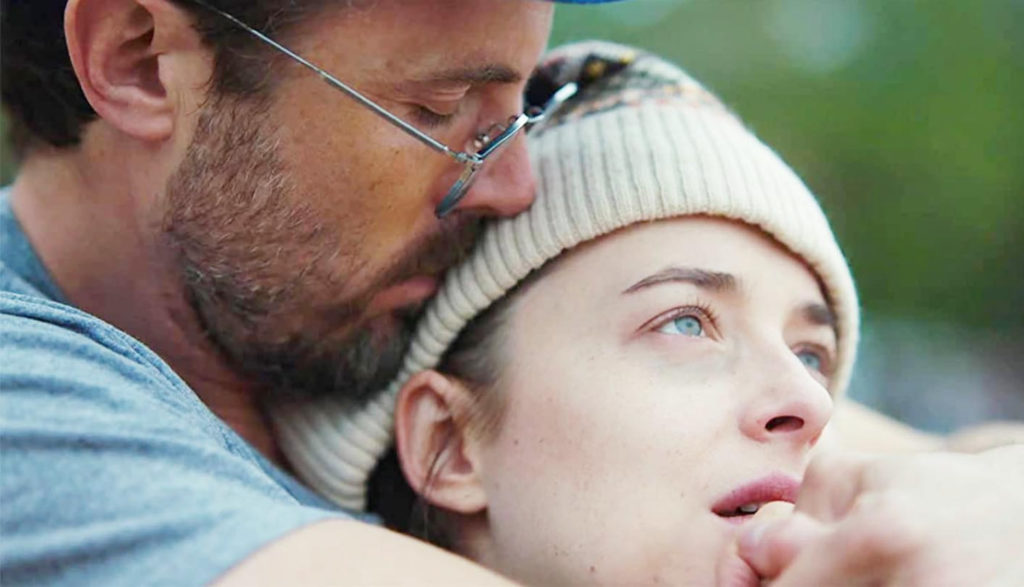 A man embraces a woman who stares upward sadly.