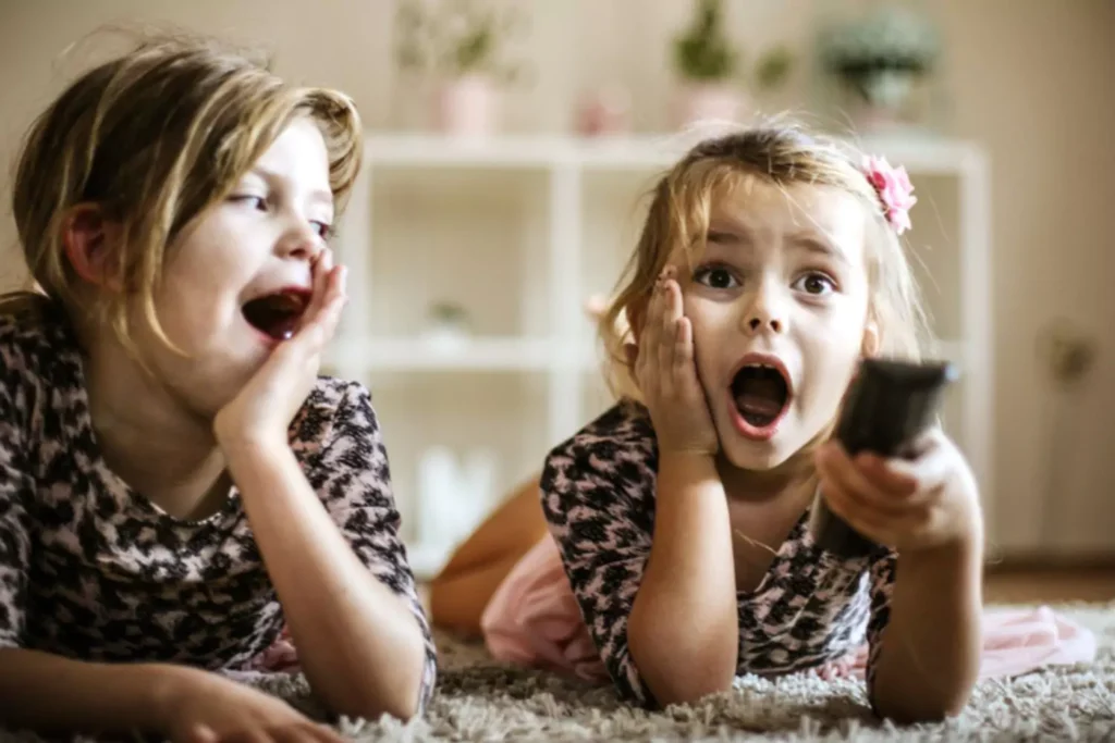 Two young girls lying on the floor looking surprised at something they're seeing on TV