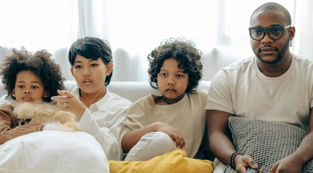 Mom, dad, and their two kids sitting on a couch, intently watching something on TV